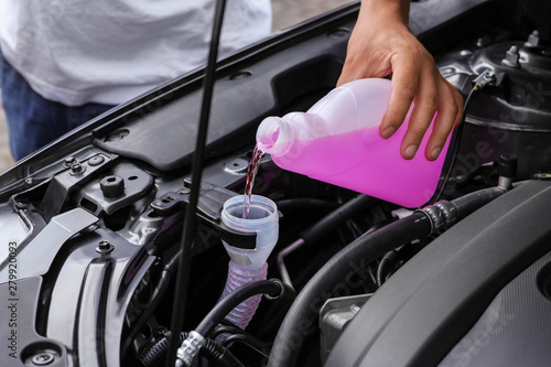 Photos Man pouring liquid from plastic canister into car washer fluid reservoir, closeu