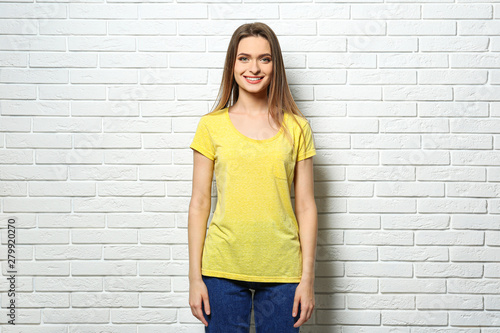 Young woman wearing blank t-shirt near white brick wall. Mockup for design