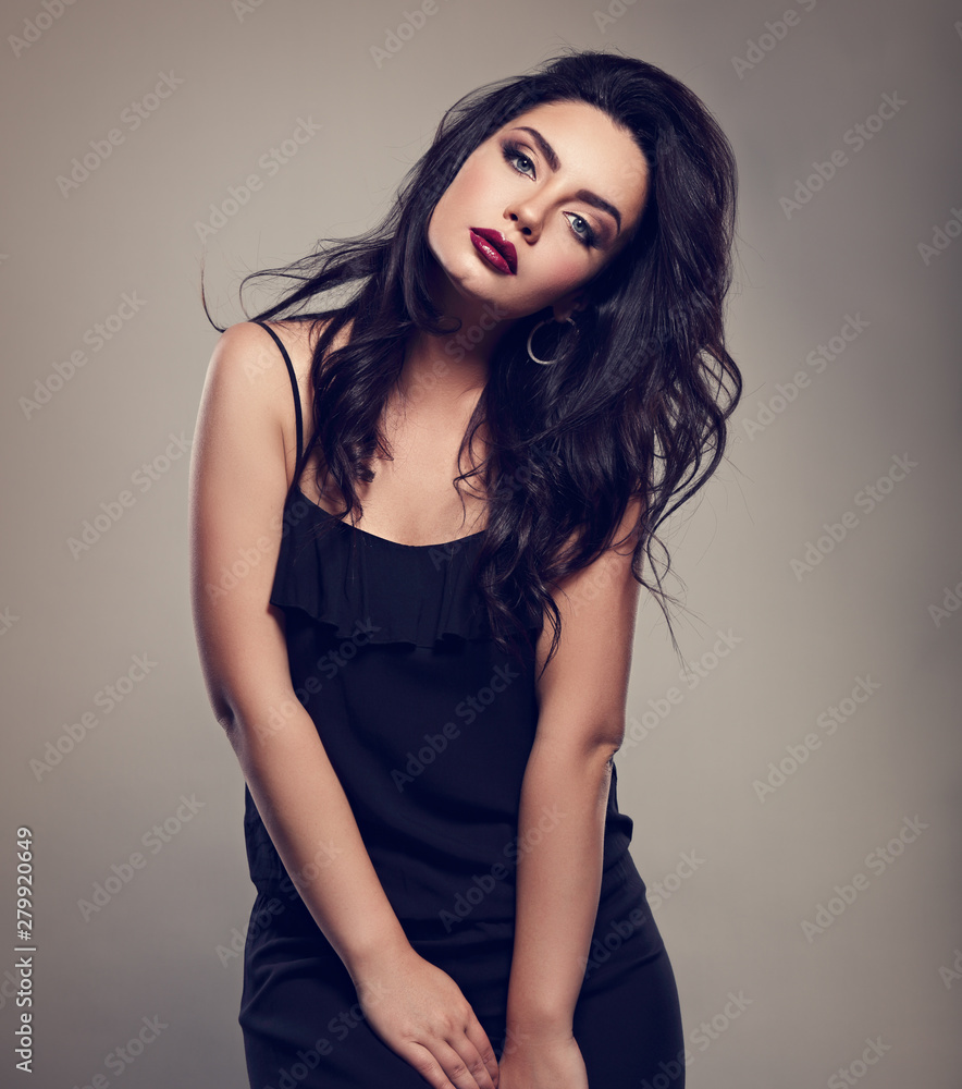 Naklejka premium Beautiful bright makeup woman with long black curly hair style in black overalls dress, burgundy lipstick with vamp look on grey background. Closeup