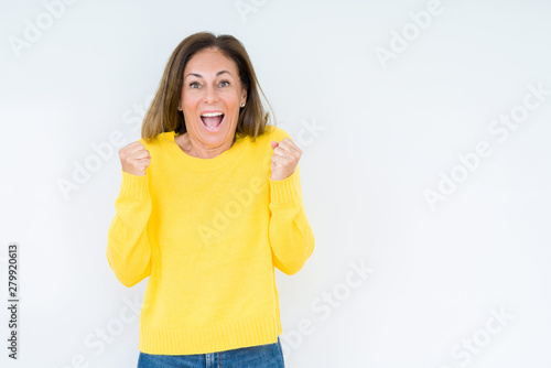 Beautiful middle age woman wearing yellow sweater over isolated background celebrating surprised and amazed for success with arms raised and open eyes. Winner concept.