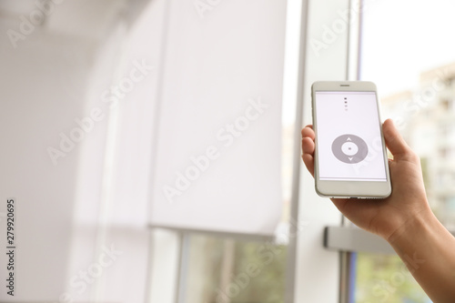 Woman using smart home application on phone to control window blinds indoors, closeup. Space for text