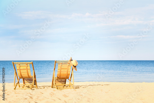 Empty wooden sunbeds with hat on sandy shore. Beach accessories