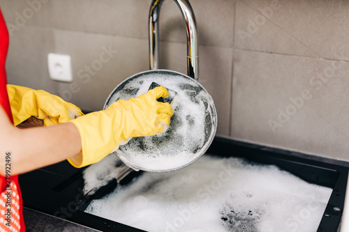 Quadro su tela Close up of woman hand in yellow protective rubber gloves washing dishes in the kitchen