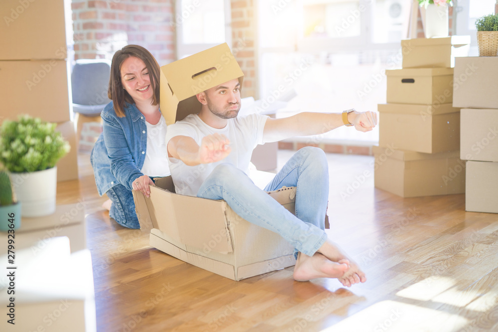 Funny and crazy couple having fun riding a cardboad box as a car, smiling happy and laughing at new home Funny and crazy couple having fun riding a cardboad box as a car, smiling happy and laughing at new home