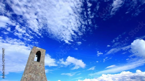 Bell tower against clouds flowing against blue sky photo