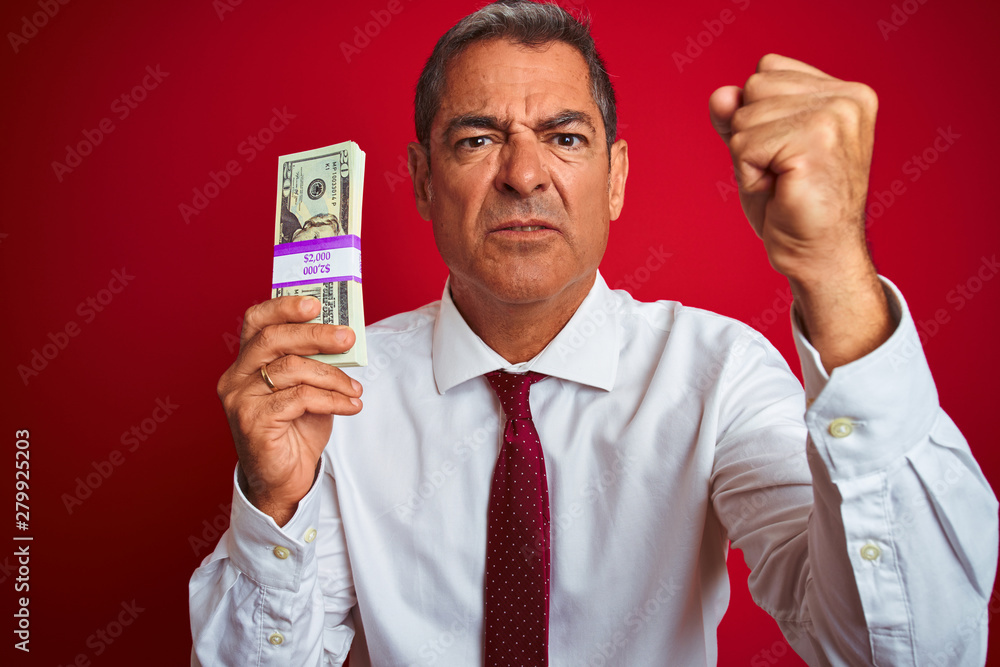 Handsome middle age businessman holding dollars over isolated red background annoyed and frustrated shouting with anger, crazy and yelling with raised hand, anger concept Handsome middle age businessman holding dollars over isolated red background annoyed and frustrated shouting with anger, crazy and yelling with raised hand, anger concept