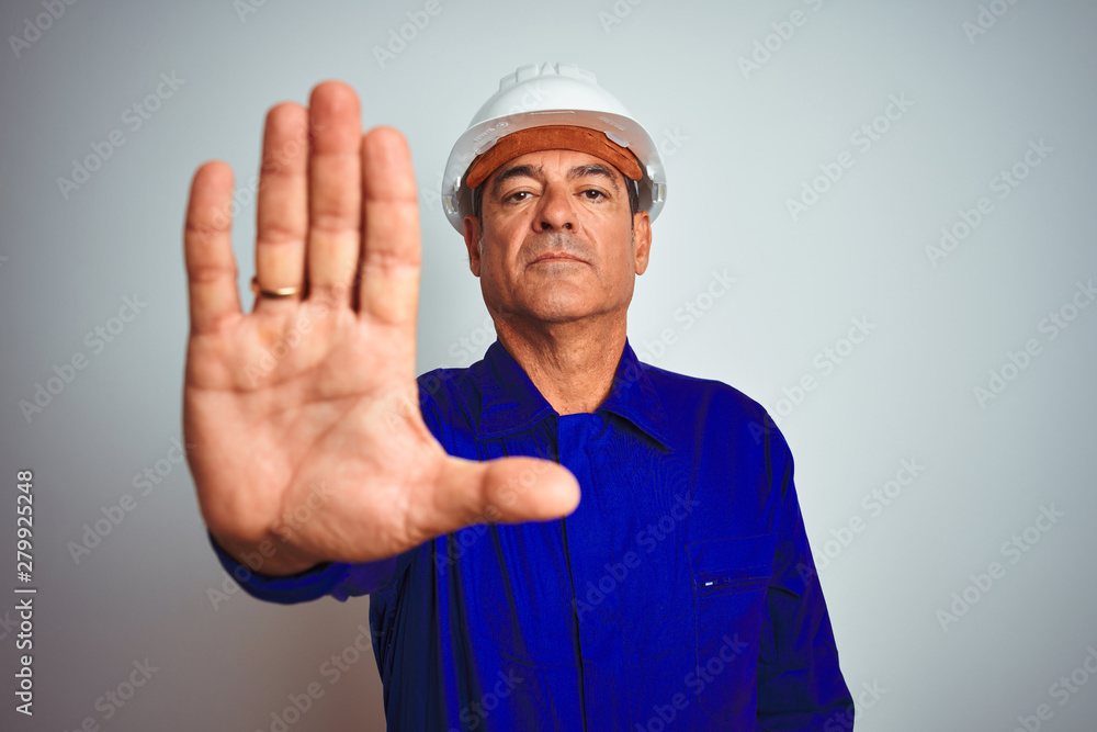 Handsome middle age worker man wearing uniform and helmet over isolated white background doing stop sing with palm of the hand. Warning expression with negative and serious gesture on the face.