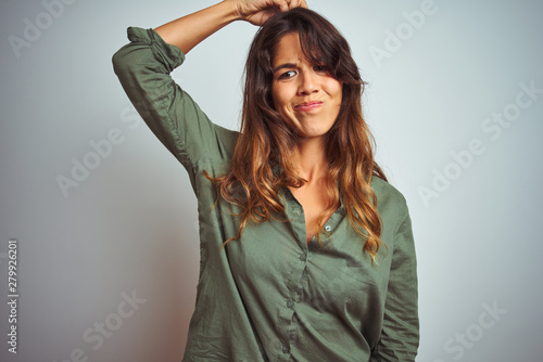 Young beautiful woman wearing green shirt standing over grey isolated background confuse and wondering about question. Uncertain with doubt, thinking with hand on head. Pensive concept.