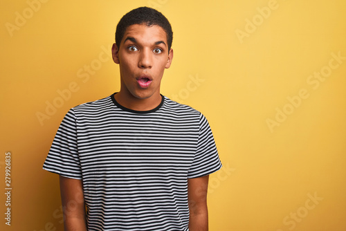 Young handsome arab man wearing navy striped t-shirt over isolated yellow background afraid and shocked with surprise expression, fear and excited face.