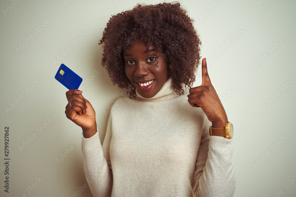 Young african afro woman holding credit card standing over isolated white background surprised with an idea or question pointing finger with happy face, number one Young african afro woman holding credit card standing over isolated white background surprised with an idea or question pointing finger with happy face, number one