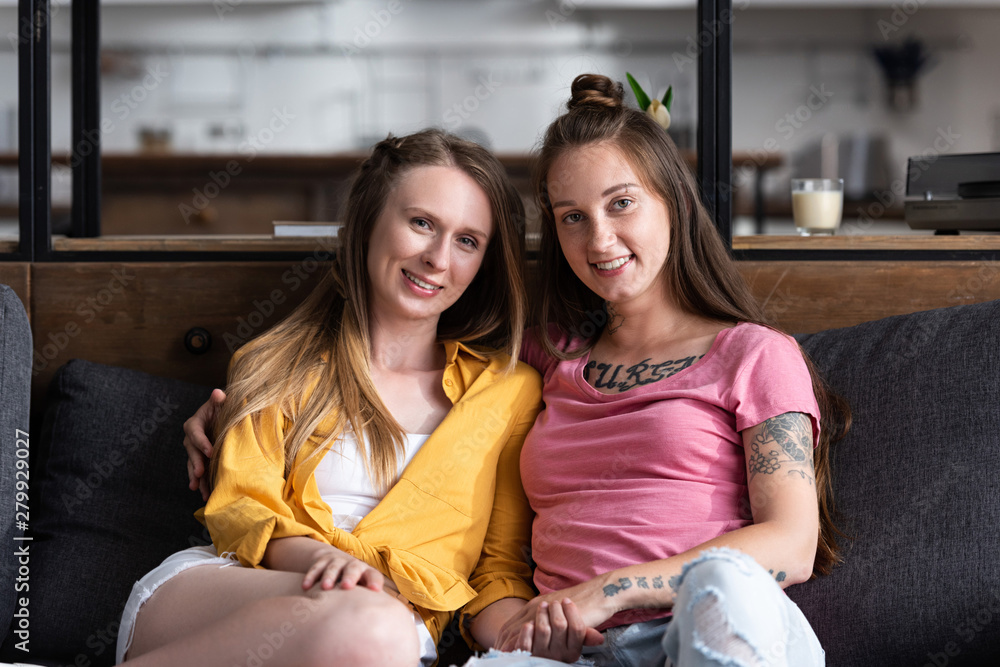 two pretty lesbians embracing while sitting on sofa in living room