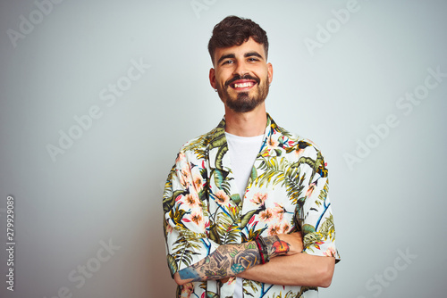 Man with tattoo on vacation wearing summer shirt standing over isolated white background happy face smiling with crossed arms looking at the camera. Positive person.