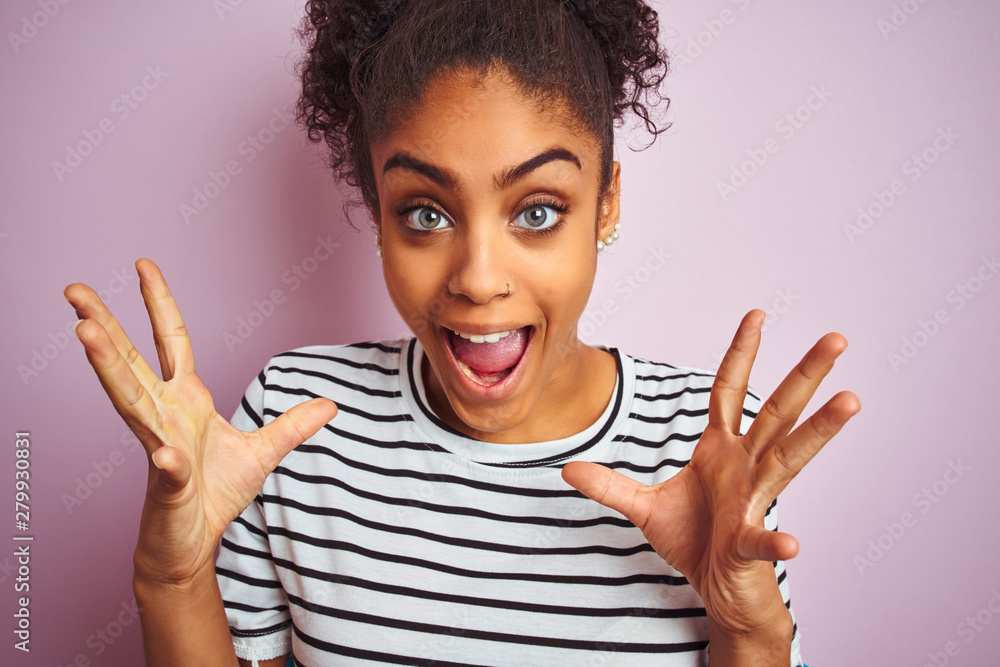 African american woman wearing navy striped t-shirt standing over isolated pink background very happy and excited, winner expression celebrating victory screaming with big smile and raised hands African american woman wearing navy striped t-shirt standing over isolated pink background very happy and excited, winner expression celebrating victory screaming with big smile and raised hands