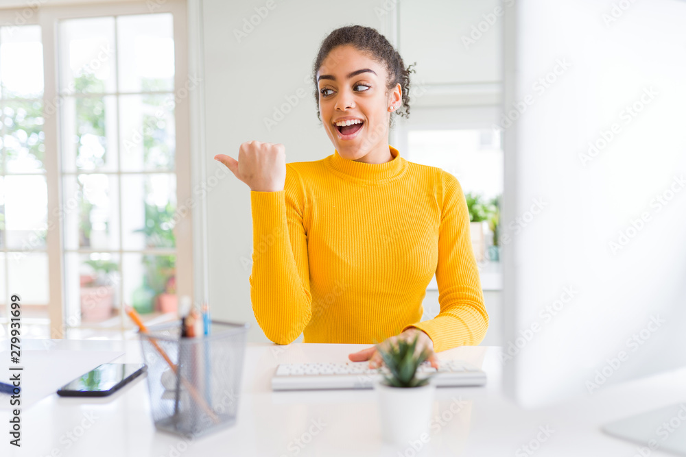 Young african american girl working using computer pointing and showing with thumb up to the side with happy face smiling Young african american girl working using computer pointing and showing with thumb up to the side with happy face smiling