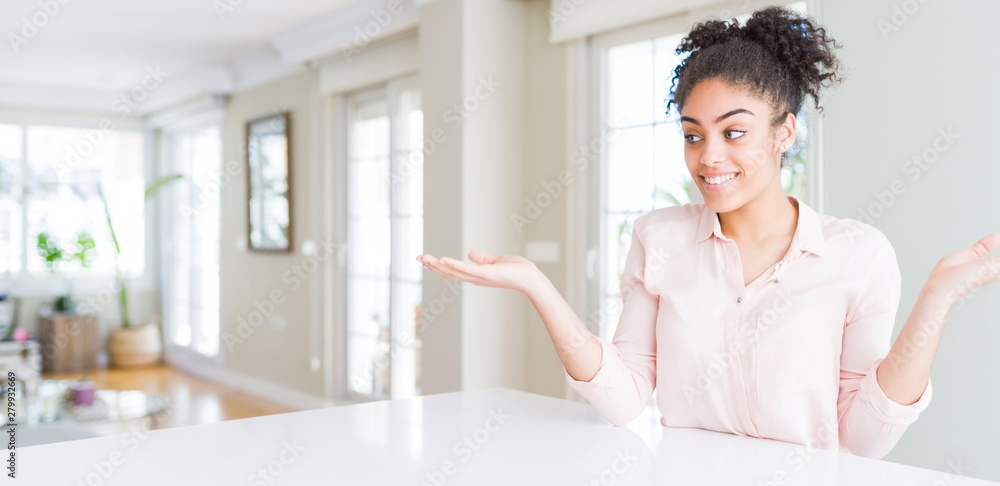 Wide angle of beautiful african american woman with afro hair smiling showing both hands open palms, presenting and advertising comparison and balance Wide angle of beautiful african american woman with afro hair smiling showing both hands open palms, presenting and advertising comparison and balance