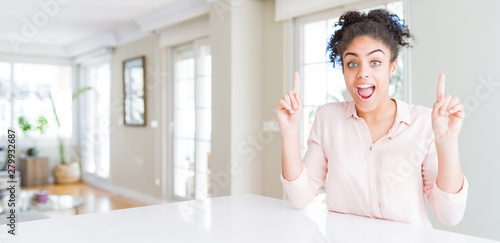 Wide angle of beautiful african american woman with afro hair smiling amazed and surprised and pointing up with fingers and raised arms.