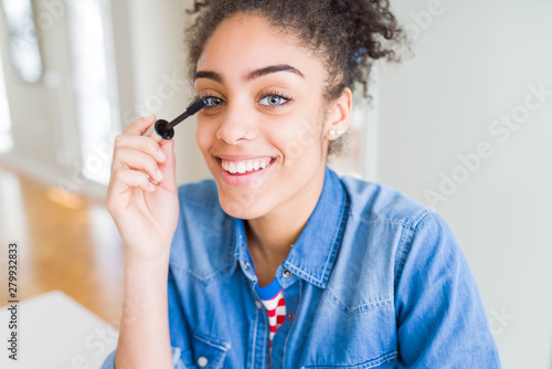 Young african american girl applying eyelashes mascara with a happy face standing and smiling with a confident smile showing teeth