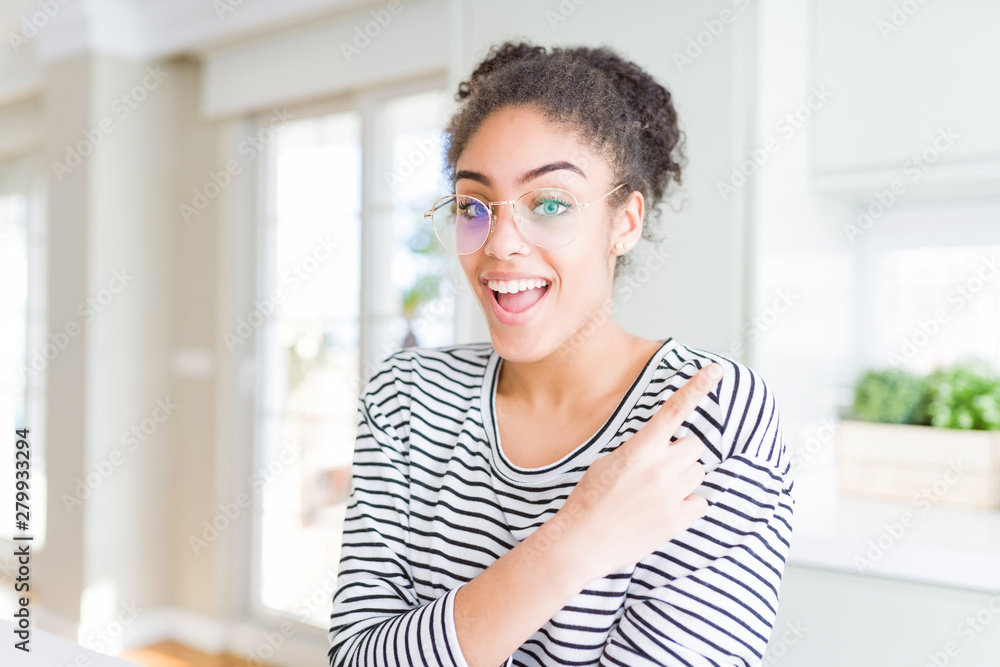 Beautiful young african american woman with afro hair wearing glasses cheerful with a smile of face pointing with hand and finger up to the side with happy and natural expression on face Beautiful young african american woman with afro hair wearing glasses cheerful with a smile of face pointing with hand and finger up to the side with happy and natural expression on face