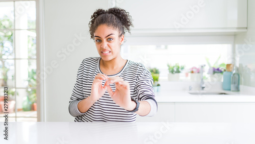 Beautiful african american woman with afro hair wearing casual striped sweater disgusted expression, displeased and fearful doing disgust face because aversion reaction. With hands raised. 