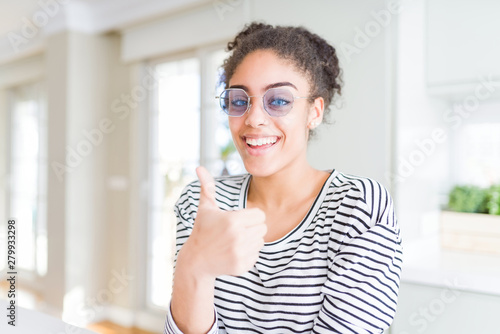 Beautiful young african american woman with afro hair wearing glasses doing happy thumbs up gesture with hand. Approving expression looking at the camera showing success. Free Download Beautiful young african american woman with afro hair wearing glasses doing happy thumbs up gesture with hand. Approving expression looking at the camera showing success. - GFXLoad