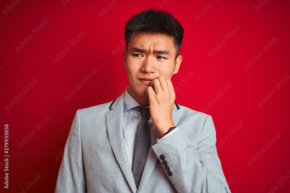 Asian chinese businessman wearing grey jacket and tie standing over isolated red background looking stressed and nervous with hands on mouth biting nails. Anxiety problem. Asian chinese businessman wearing grey jacket and tie standing over isolated red background looking stressed and nervous with hands on mouth biting nails. Anxiety problem.