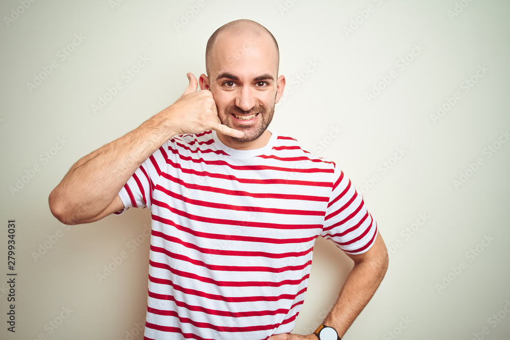 Young bald man with beard wearing casual striped red t-shirt over white isolated background smiling doing phone gesture with hand and fingers like talking on the telephone. Communicating concepts. Young bald man with beard wearing casual striped red t-shirt over white isolated background smiling doing phone gesture with hand and fingers like talking on the telephone. Communicating concepts.