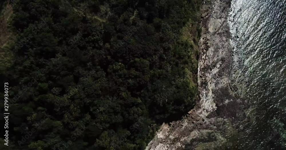 Drone flies above green rocky island top against waves crashing at rocks Drone flies above green rocky island top against waves crashing at rocks