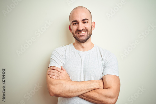 Canvastavla Young bald man with beard wearing casual white t-shirt over isolated background happy face smiling with crossed arms looking at the camera