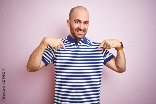 Young bald man with beard wearing casual striped blue t-shirt over pink isolated background looking confident with smile on face, pointing oneself with fingers proud and happy.