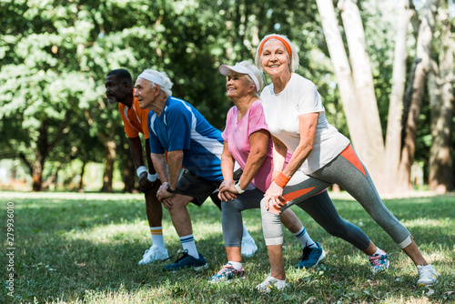 selective focus of happy senior and multicultural people doing stretching exercise on grass