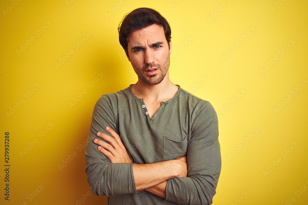 Young handsome man wearing casual t-shirt standing over isolated yellow background skeptic and nervous, disapproving expression on face with crossed arms. Negative person. Young handsome man wearing casual t-shirt standing over isolated yellow background skeptic and nervous, disapproving expression on face with crossed arms. Negative person.