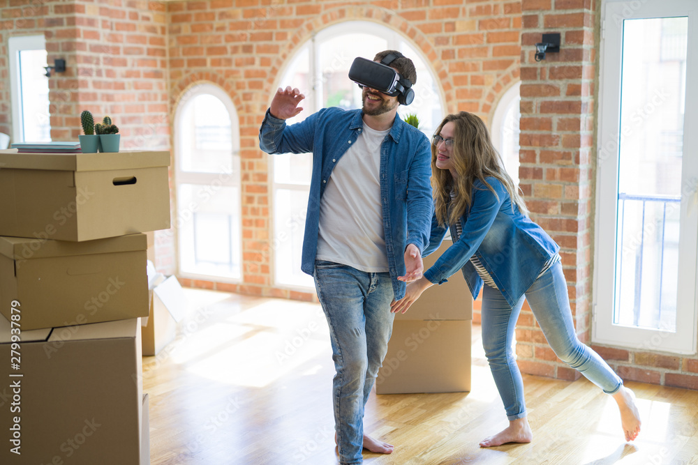 Young couple moving to a new house having fun playing with virtual reality glasses around cardboard boxes Young couple moving to a new house having fun playing with virtual reality glasses around cardboard boxes