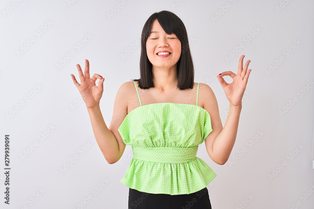 Young beautiful chinese woman wearing green t-shirt over isolated white background relax and smiling with eyes closed doing meditation gesture with fingers. Yoga concept. Young beautiful chinese woman wearing green t-shirt over isolated white background relax and smiling with eyes closed doing meditation gesture with fingers. Yoga concept.