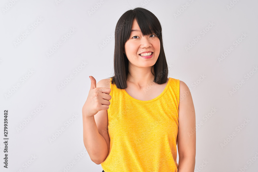 Young beautiful chinese woman wearing yellow t-shirt over isolated white background doing happy thumbs up gesture with hand. Approving expression looking at the camera with showing success. Young beautiful chinese woman wearing yellow t-shirt over isolated white background doing happy thumbs up gesture with hand. Approving expression looking at the camera with showing success.