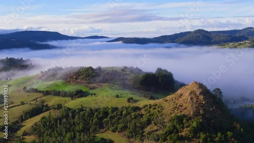 Aerial view at low altitude during the morning with low clouds advancing surrounding a small hill 