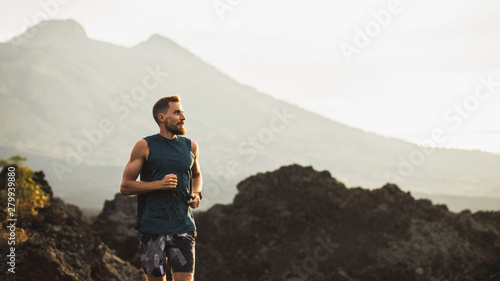 Young athlete man trail running in mountains in the morning. Healthy lifestyle concept. Panoramic photo with empty copy space.