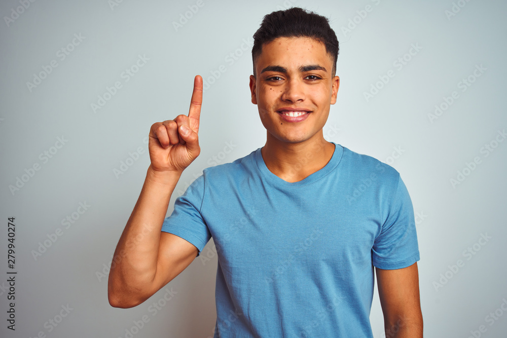 Φωτογραφία Young brazilian man wearing blue t-shirt standing over isolated white background showing and pointing up with finger number one while smiling confident and happy