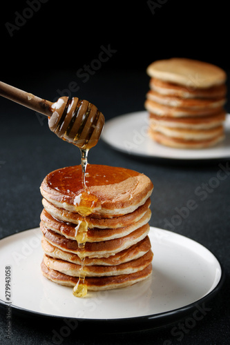Stack of Pancakes with pouring honey on dark background. honey spoon