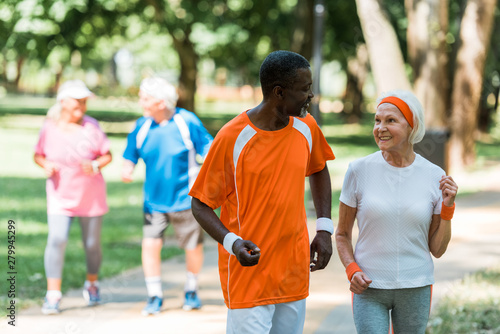 selective focus of african american senior man and cheerful retired woman exercising near pensioners outside