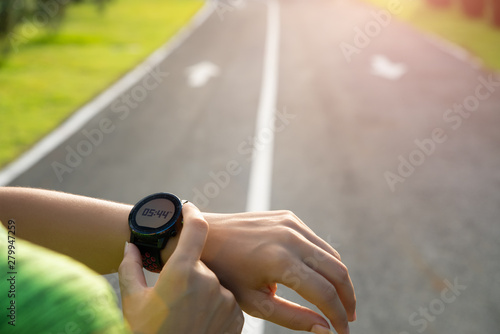 Young fitness woman runner setting up smart watch before running training during sunset. Outdoor exercise activities concept.