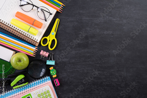 Education or back to school Concept. Top view of Colorful school supplies with books, color pencils, calculator, pen cutter clips and green apple on chalkboard background. Flat lay.