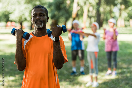selective focus of senior african american man holding dumbbells while exercising in park