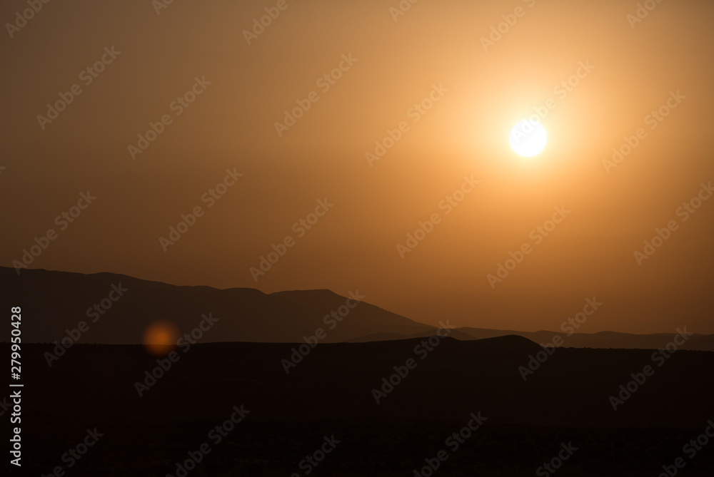Morning landscape with mountains and orange sky at sunrise with sun reflecting. Evening sunset on the horizon of hills