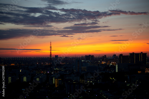 Silhouette of antenna tower in the city with light of sunrise and clouded sky in background