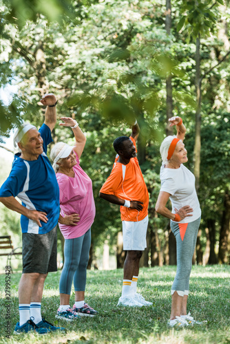 selective focus of cheerful multicultural senior men and women standing with hands on hips while doing exercise