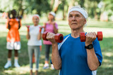 selective focus of senior man with grey hair holding dumbbells in park