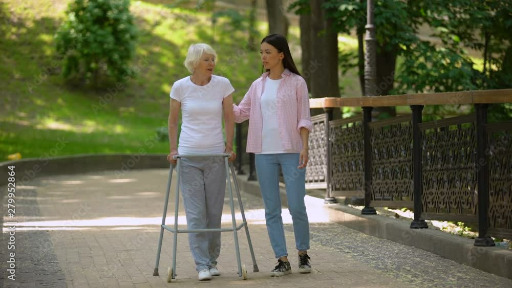 Woman supporting disabled elderly grandmother, walking in hospital park, illness Woman supporting disabled elderly grandmother, walking in hospital park, illness