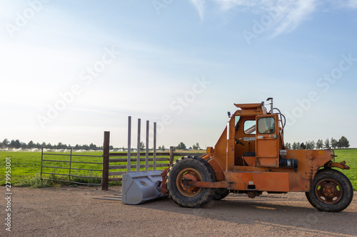 Side angle of orange tractor with a plow in a field with blue sky in the background photo