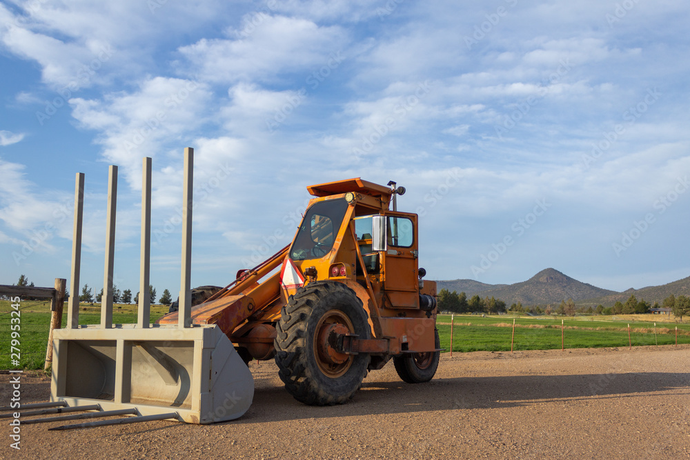 Side angle of orange tractor with a plow in a field with blue sky in the background Side angle of orange tractor with a plow in a field with blue sky in the background