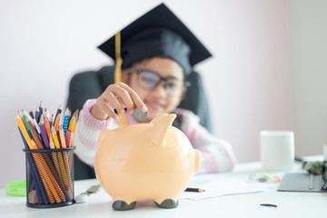 Little Asian girl putting the coin into piggy bank and smile with happiness for money saving to wealthness in the future of education concept select focus shallow depth of field